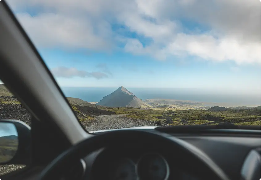 Vue aérienne de la côte pittoresque de l'Islande et des routes sinueuses, mettant en valeur les vastes paysages accessibles avec une voiture de location le long de la Route circulaire.