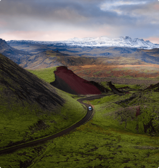 Scenic drive through Icelandic highlands with a van navigating winding roads surrounded by mossy green landscapes and volcanic hills.