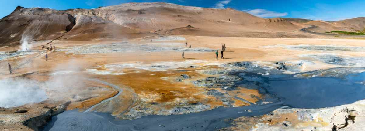 Panoramic view of the Icelandic geothermal area Hverir with a myriad of colors in its terrain enhanced by the blue sky that accompanies visitors.