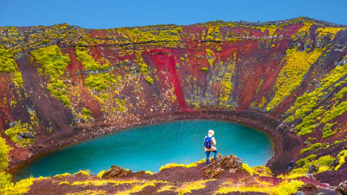 A hiker defies danger in Iceland's majestic and colorful Kerid crater by walking on its surface.