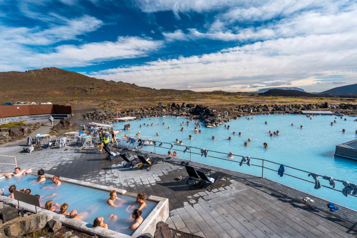 Dozens of bathers enjoy a thermal bath in the waters of Myvatn in Iceland under partly clear skies.