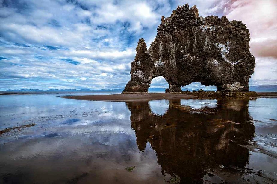 Hv&iacute;tserkur, una llamativa formaci&oacute;n rocosa que se asemeja a un drag&oacute;n o dinosaurio bebiendo del mar, reflejada en las tranquilas aguas durante la marea baja en Islandia.