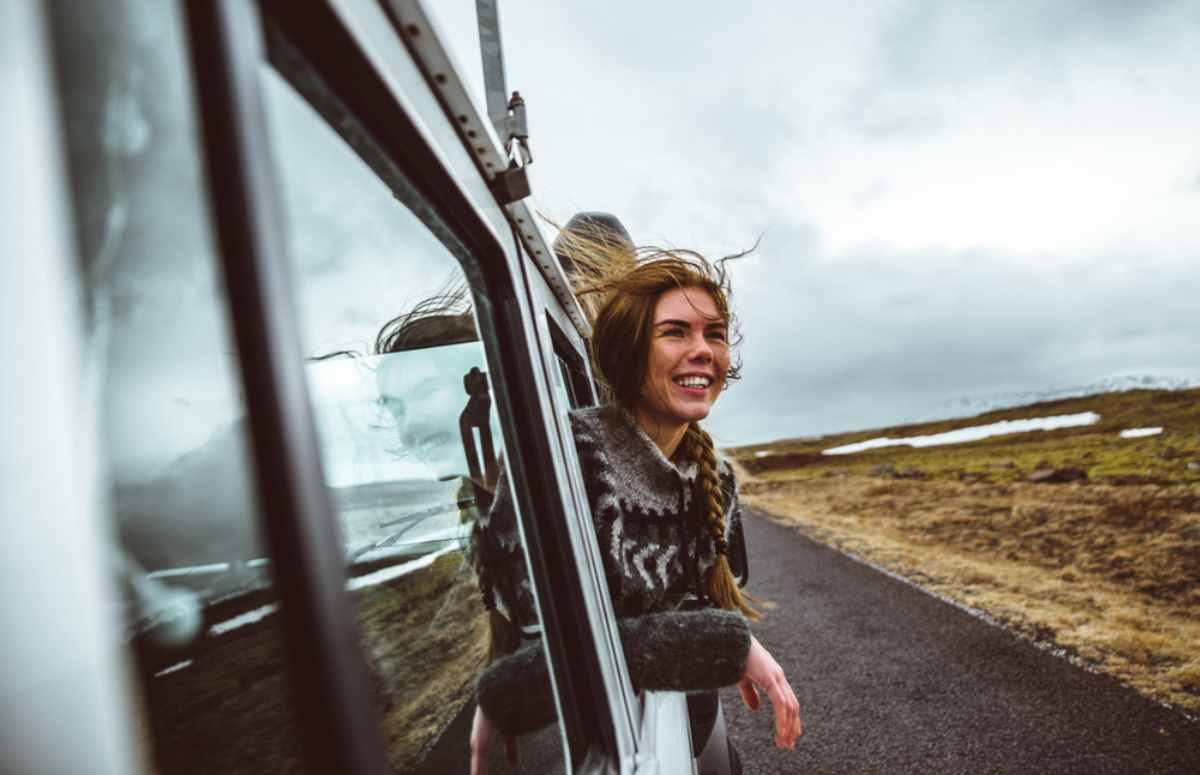 Turista asom&aacute;ndose por la ventanilla de su coche de alquiler disfrutando del viento y de los paisajes de Islandia