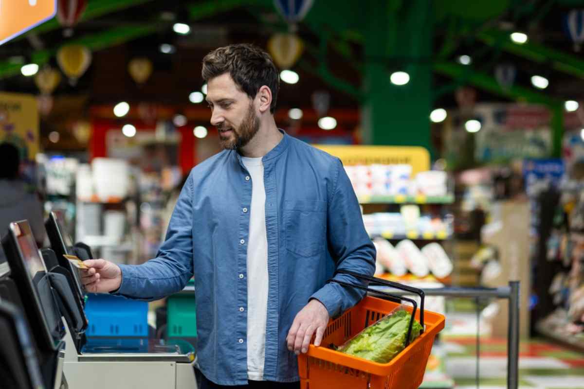 Man using a self-checkout machine at a supermarket in Iceland, holding a shopping basket.