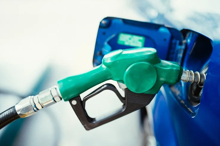 Vue rapprochée d’un pistolet vert de pompe à essence remplissant une voiture bleue, mettant en évidence le processus de ravitaillement à une station-service.