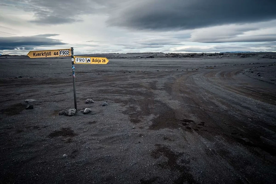 Un panneau solitaire à un carrefour désert dans un vaste paysage aride, sol volcanique sombre sous un ciel couvert, indiquant Kverkfjöll et Askja en Islande.