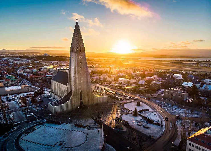 Vista aerea della chiesa di Hallgrímskirkja a Reykjavik, in Islanda, all'alba, con il sole che proietta una calda luce dorata sul paesaggio urbano e sui tetti spolverati di neve.