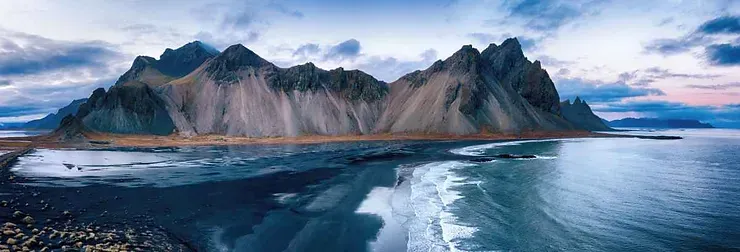 Vue panoramique de la montagne Vestrahorn sur la péninsule islandaise de Stokksnes, avec ses pics spectaculaires, ses plages de sable noir et les eaux calmes et bleues de l'océan Atlantique.