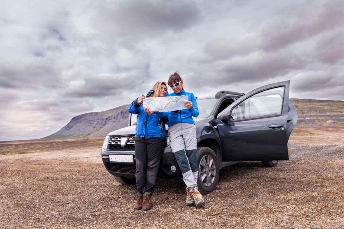 Flexibility in Iceland while driving a rental car Two travelers standing beside a rental SUV in Iceland while checking a paper map under a cloudy sky