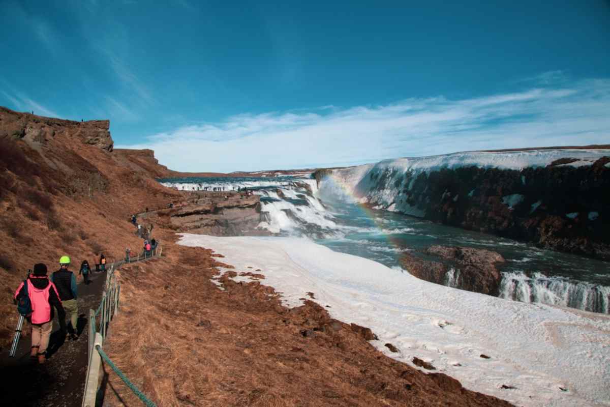 Golden Circle tour Visitors walking along the trail beside Gullfoss waterfall in Iceland with patches of snow on the ground
