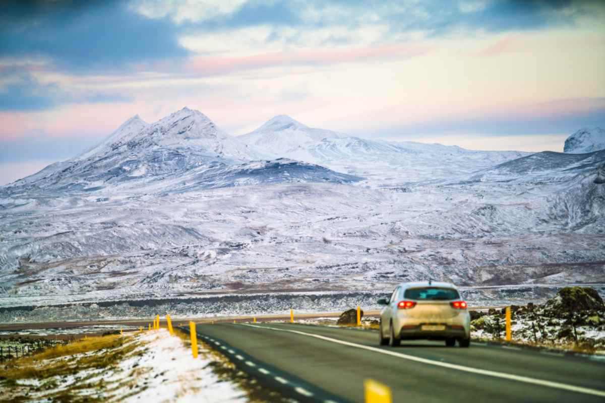 Driving the Ring Road in Iceland Car driving on an open road in Iceland with snow-covered mountains in the background