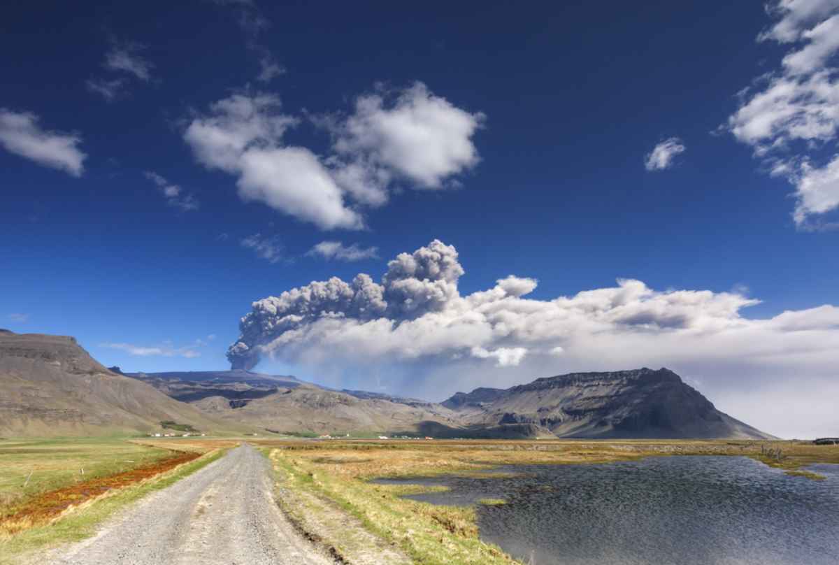 Carretera que conduce al volc&aacute;n Eyjafjallajokull con una columna de ceniza y un panache