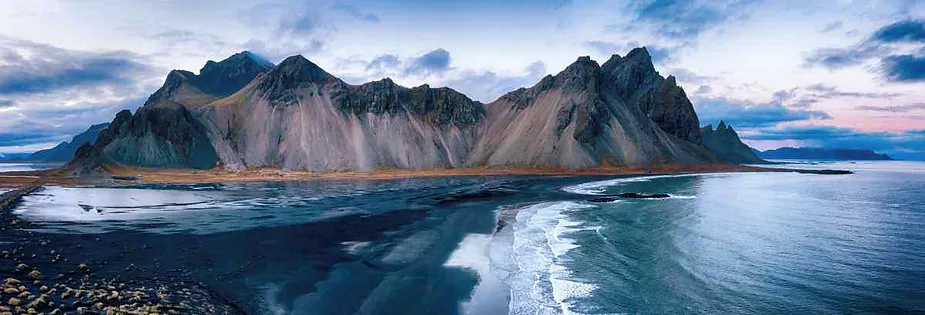 Panoramablick auf den Berg Vestrahorn auf der isl&auml;ndischen Halbinsel Stokksnes mit ihren dramatischen Gipfeln, schwarzen Sandstr&auml;nden und dem ruhigen blauen Wasser des Atlantiks.