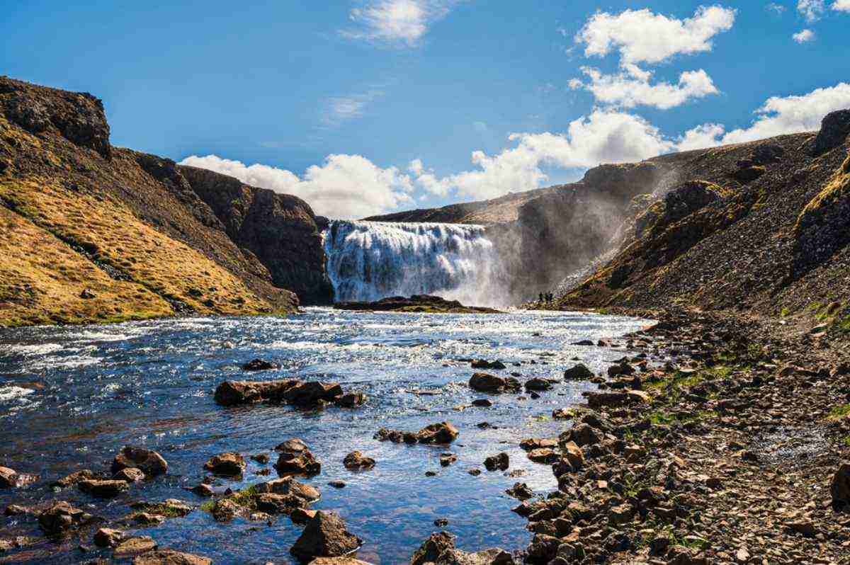 Vista general de la cascada Thorufoss de Islandia con un largo chorro de agua y un d&iacute;a soleado.