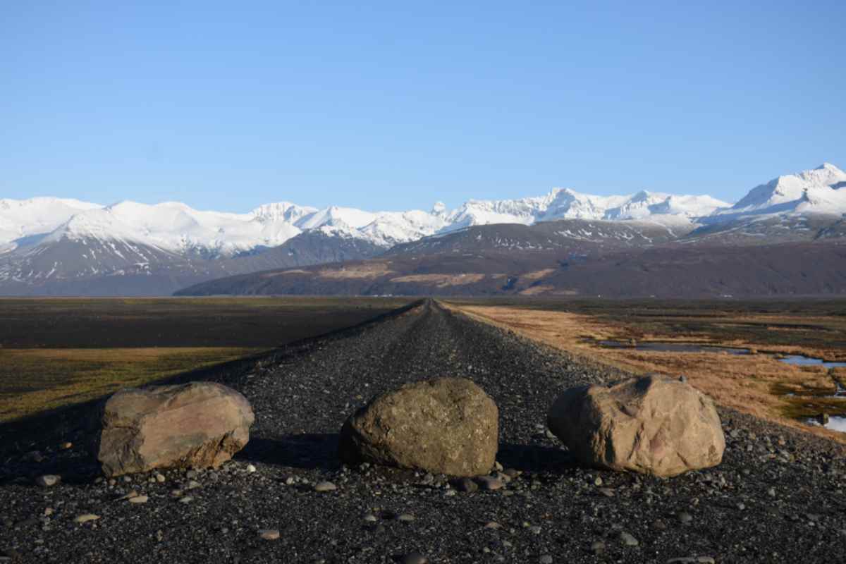 Drei strategisch platzierte Felsen blockieren den Weg zu einer verlassenen Straße, die zu Islands massiven, schneebedeckten Bergen führt.