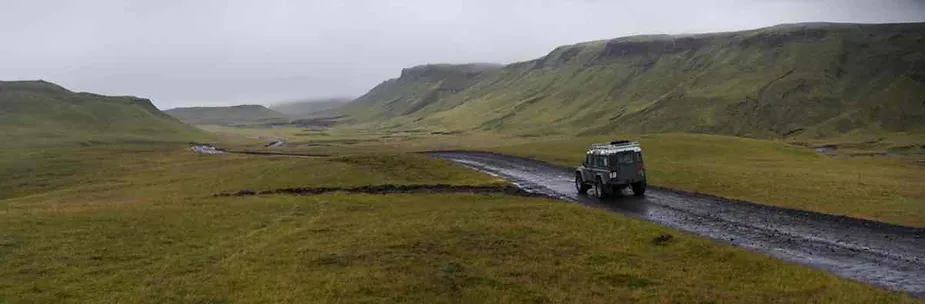 Un robusto veicolo 4x4 percorre una strada sterrata in una zona remota delle ampie highlands verdi dell'Islanda sotto un cielo nuvoloso. L'immagine evidenzia la guida off-road nel terreno aspro dell'Islanda.