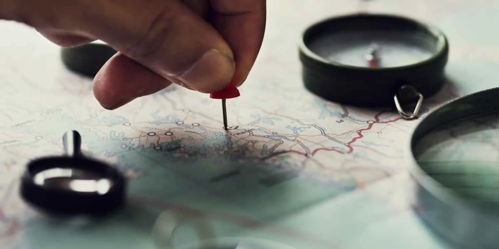 Primo piano di una mano che posiziona una puntina rossa su una mappa dettagliata.