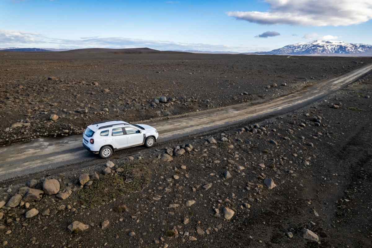 White SUV rental car on a lonely gravel road across Iceland’s volcanic highlands.