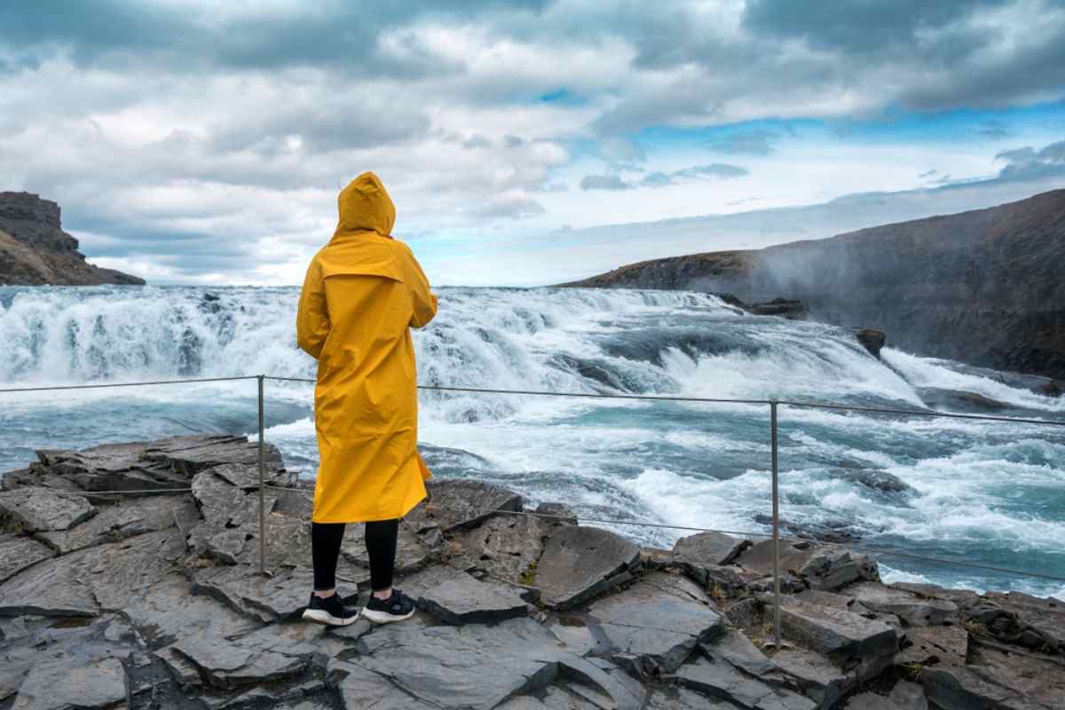 Traveler in a yellow raincoat looking at the powerful Gullfoss waterfall in Iceland.