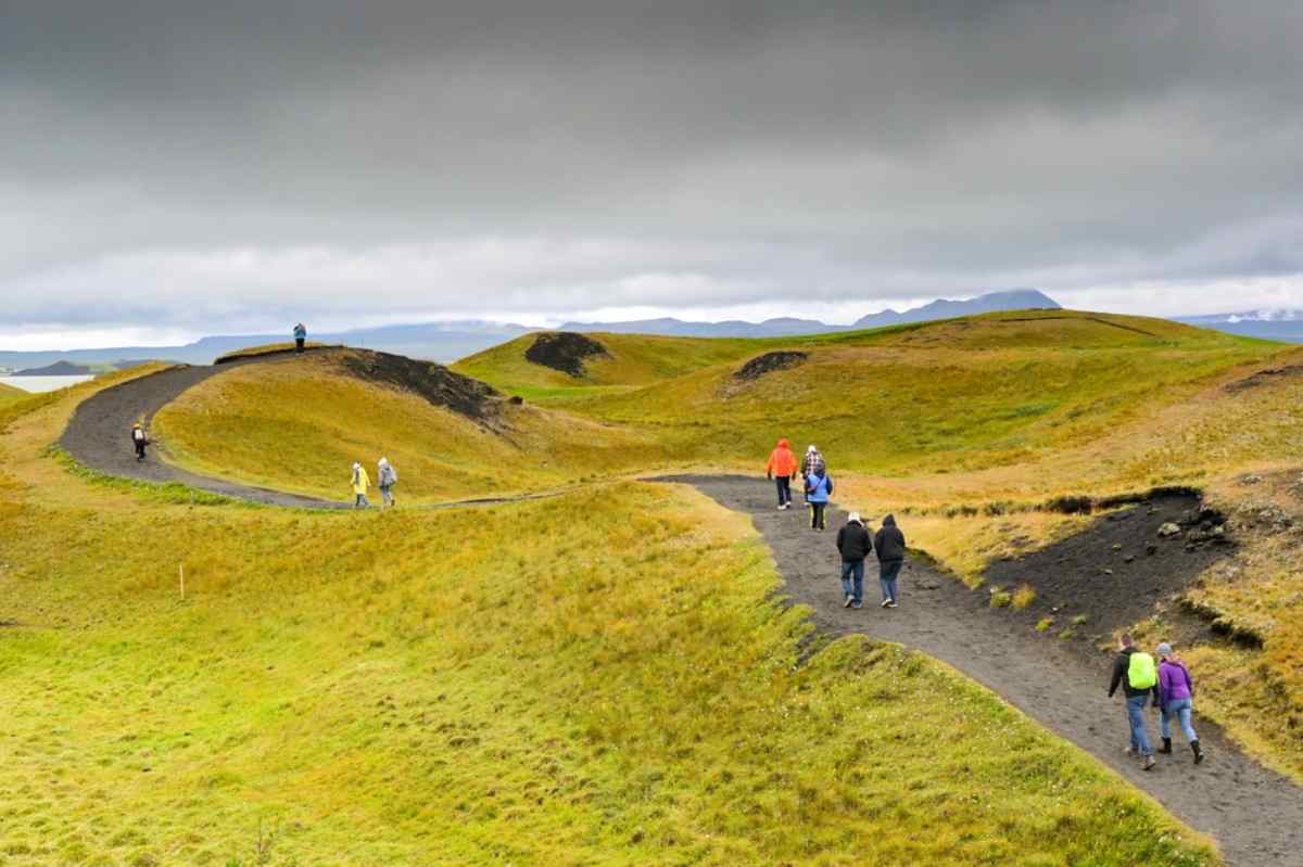 Tourists walking along lava fields and green paths near Lake Mývatn in North Iceland.