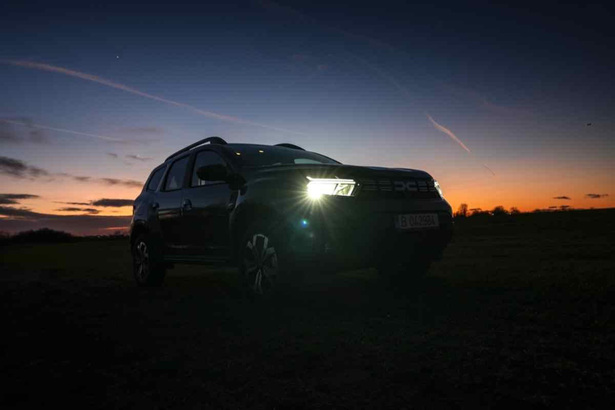 Mietwagen Dacia Duster mit eingeschaltetem Licht in der Dämmerung vor einem farbigen isländischen Sonnenuntergang.