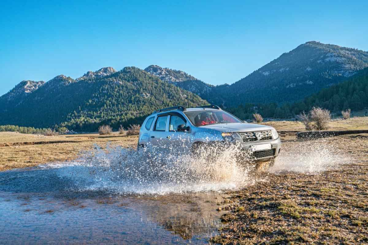 4x4-Mietwagen spritzt beim Durchfahren eines seichten Flusses in Island, Berge im Hintergrund.