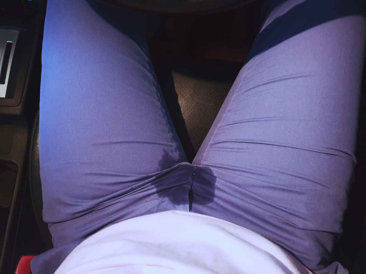 Man with a stain of pee in his crotch while sitting on the car