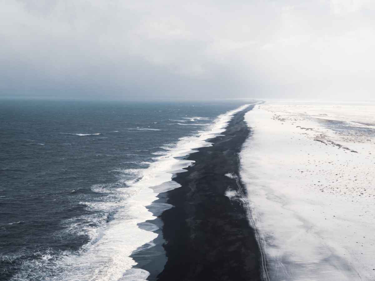 Impressive views of a black sand beach with snow from Dyrholaey