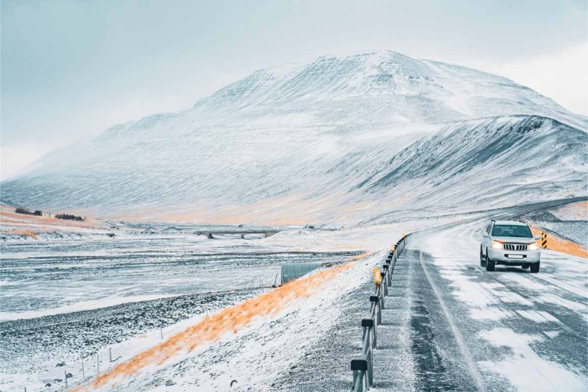 Car driving along a snowy road in Iceland, with snow-covered mountains in the background and crisp winter light.