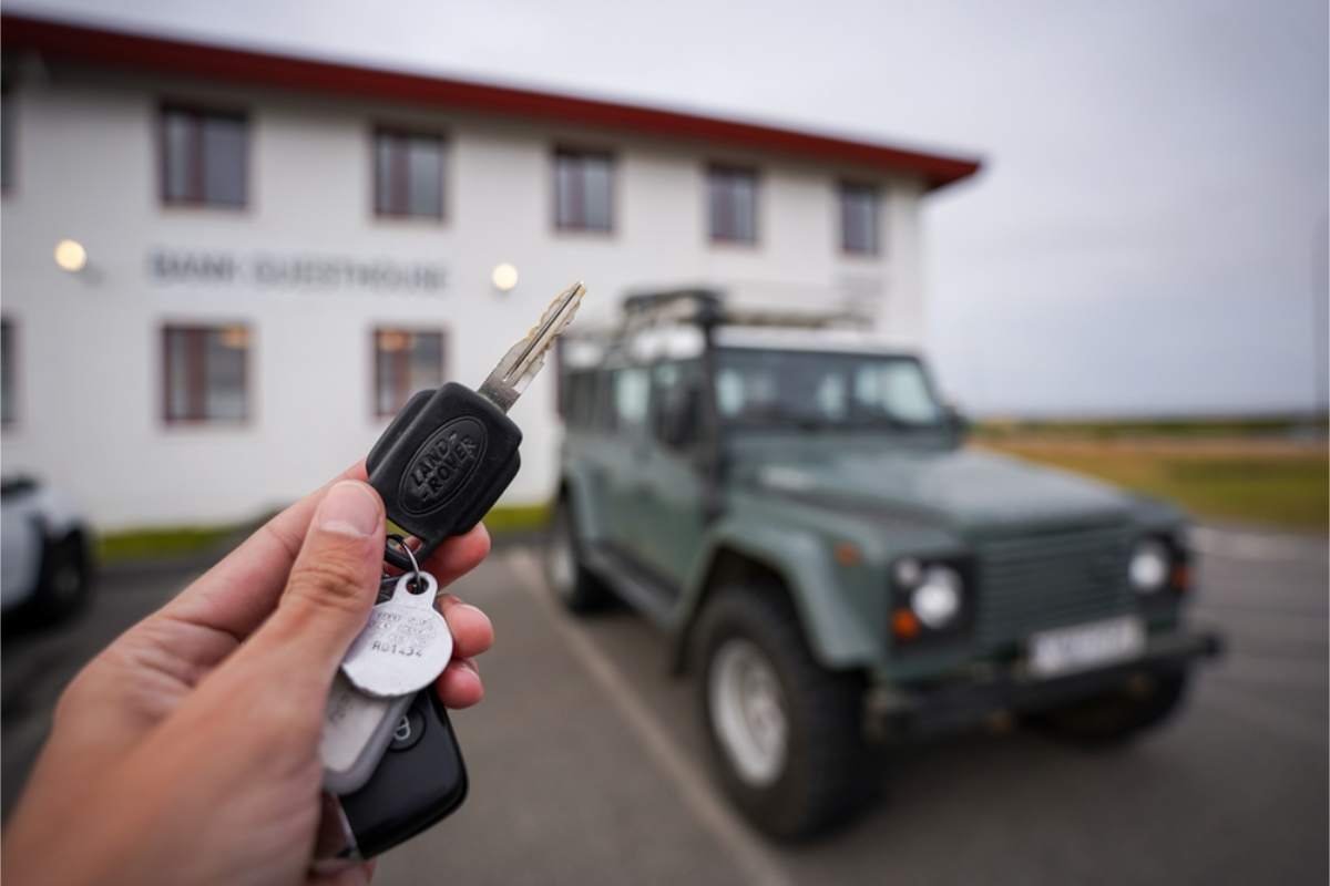 Hand holding Land Rover keys in front of a 4x4 rental vehicle in Iceland