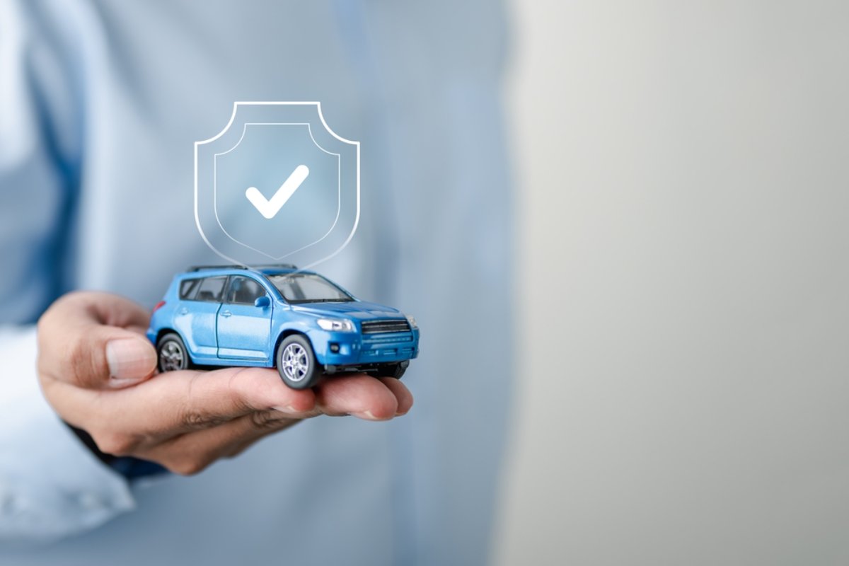 Hand holding a blue toy car with a shield icon, symbolizing car rental insurance in Iceland