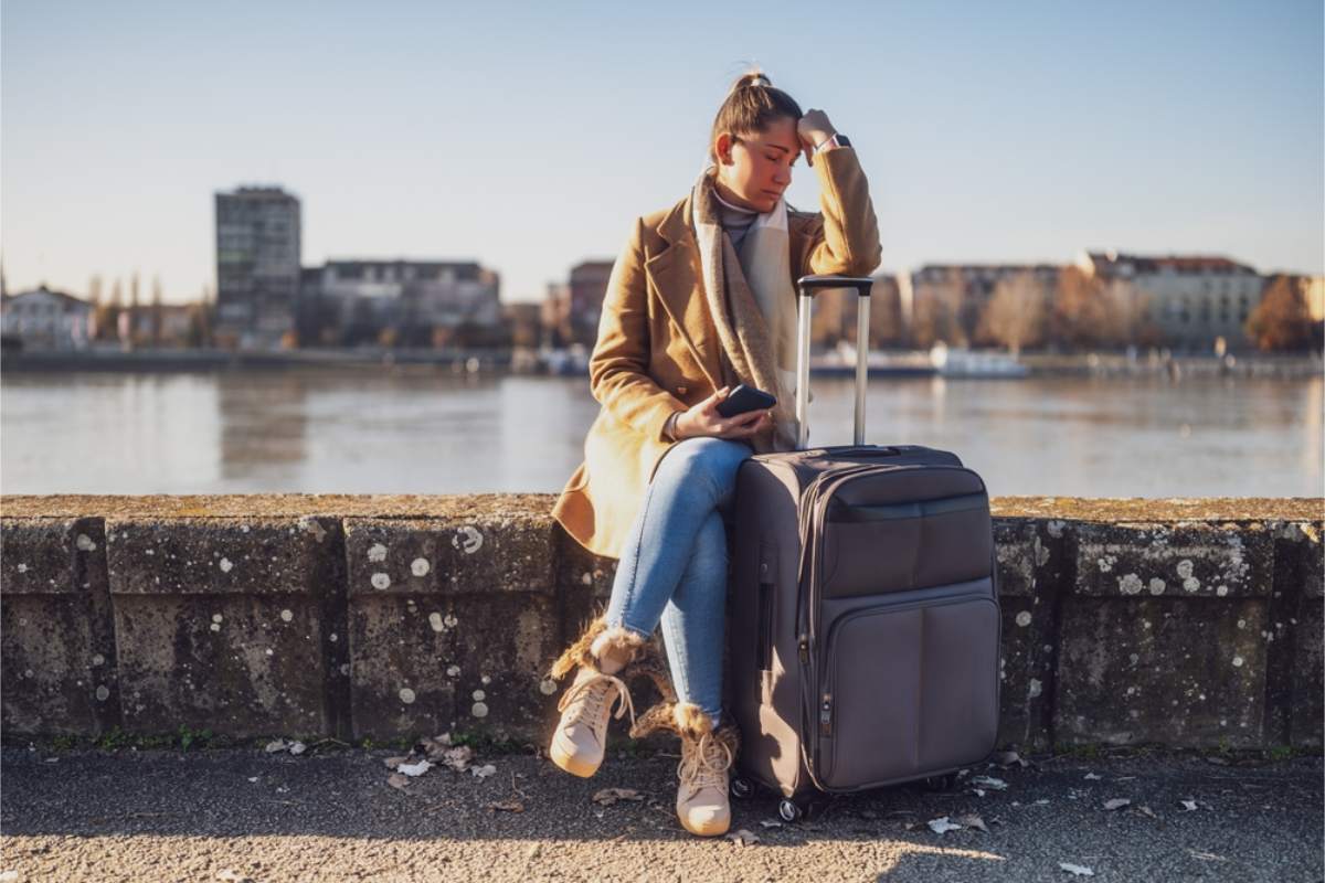 Traveler sitting with a suitcase looking stressed after being refused a rental car