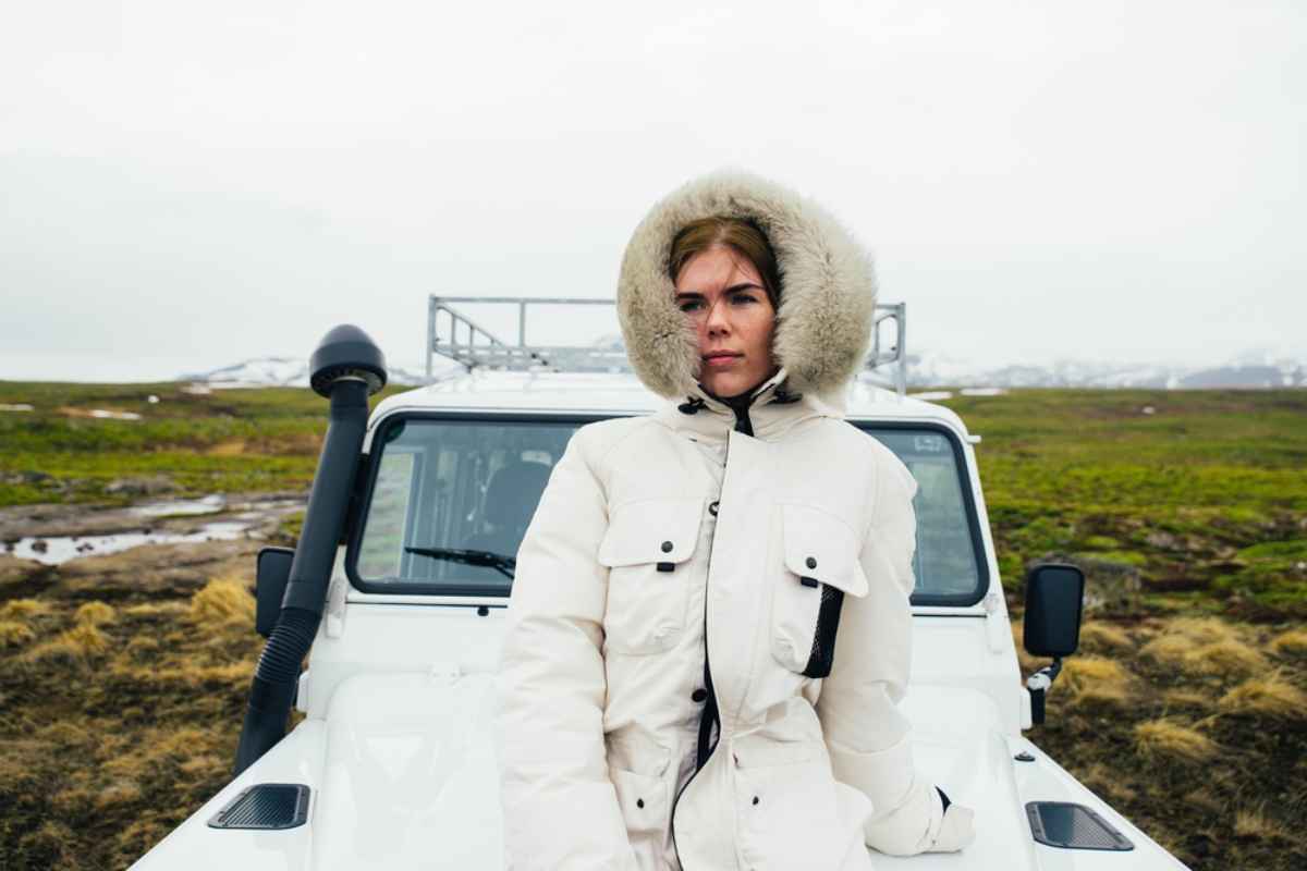 Traveler in a white winter jacket standing in front of a 4x4 vehicle in the Icelandic countryside
