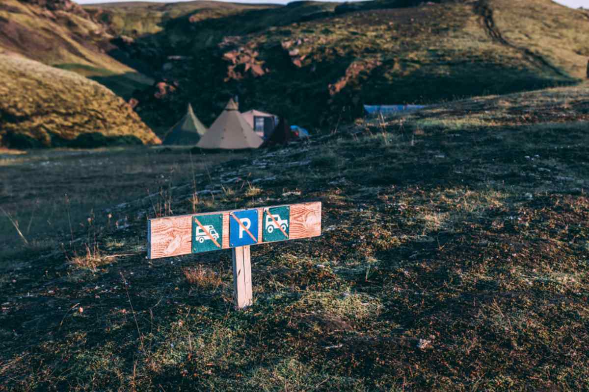 Wooden sign in a mossy Icelandic valley showing no camping and no parking symbols near a remote campsite.