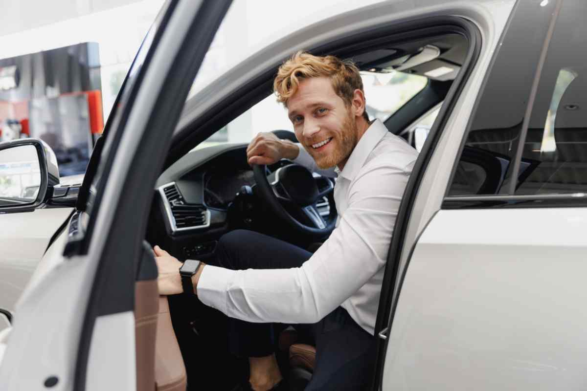 Smiling man sitting in the driver&rsquo;s seat of a white SUV with the door open, looking back toward the camera.Smiling man sitting in the driver&rsquo;s seat of a white SUV with the door open, looking back toward the camera.