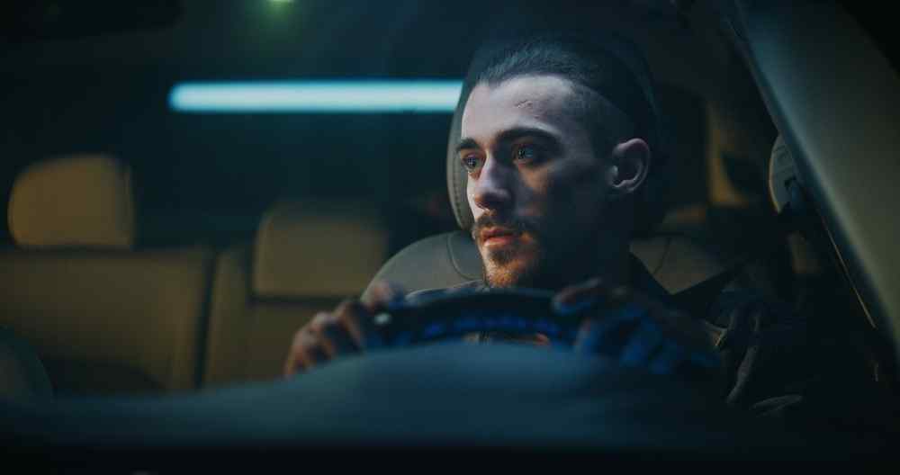 Man driving a car at night, seen through the windshield.