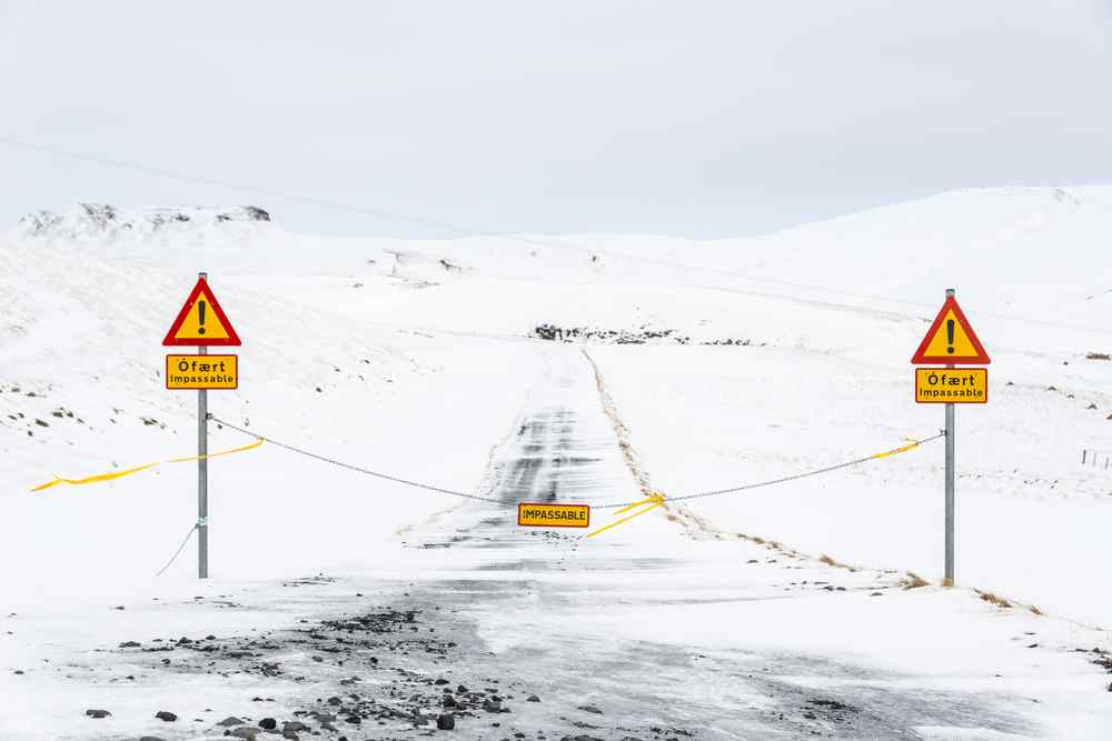 Snow-covered road in Iceland closed with signs marking it as impassable.
