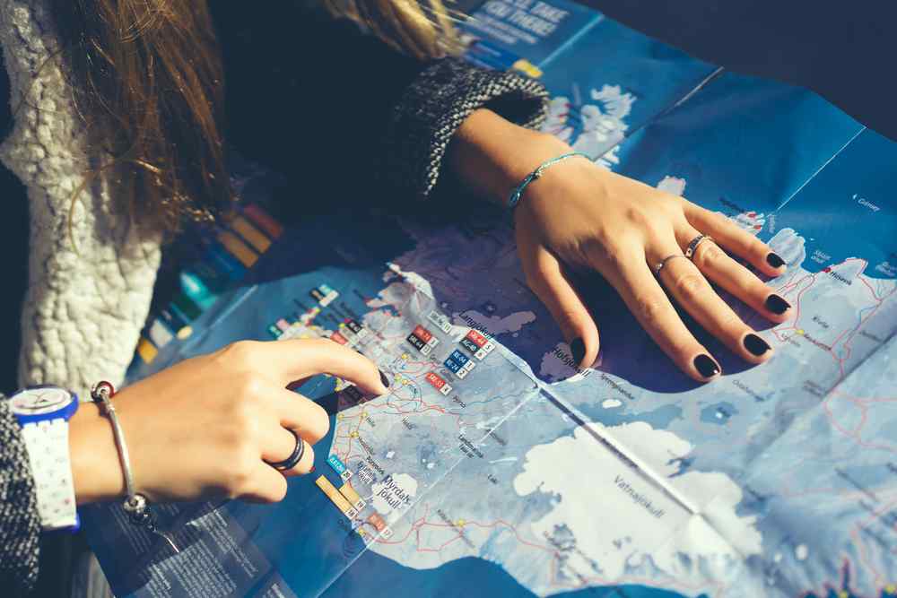 Traveler pointing to a route on a paper map of Iceland.