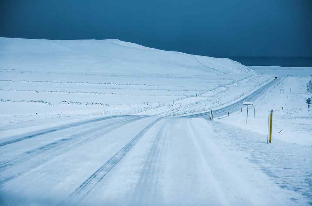 Icy rural road crossing a snow-covered Icelandic landscape under a dark sky.