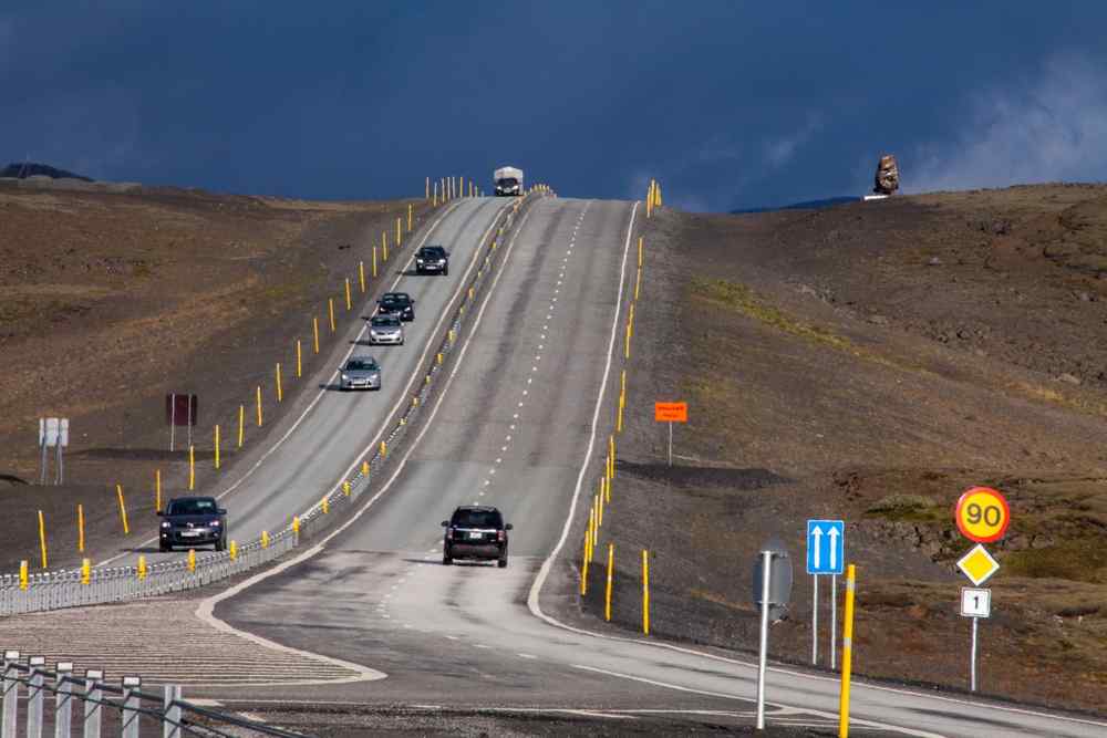 Cars travelling along Iceland’s Route 1 past a 90 km/h speed limit sign in a remote volcanic landscape.