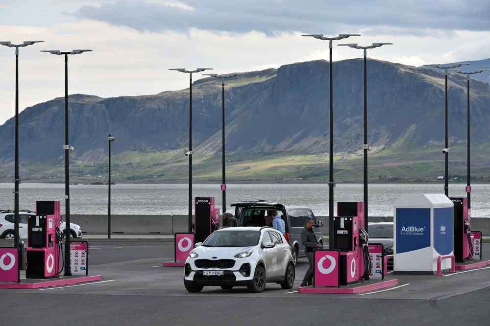 Iceland's gas station Cars refuelling at a modern gas station in Iceland, with the sea and rugged mountains visible in the background.