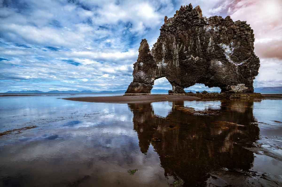 Hvítserkur, eine markante Felsformation, die an einen aus dem Meer trinkenden Drachen oder Dinosaurier erinnert, spiegelt sich im ruhigen Wasser bei Ebbe in Island.