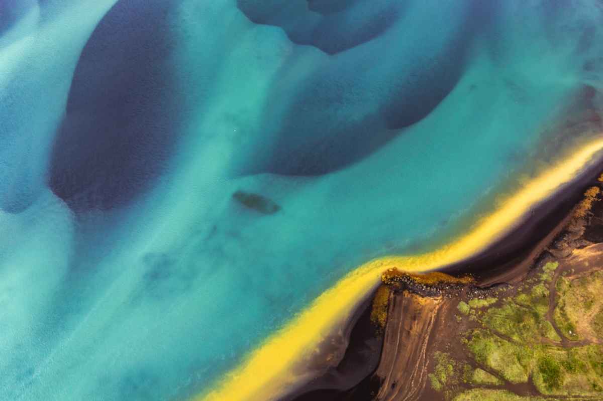 Gelbe, grüne Felder, schwarzer Sand und blaues Wasser in Island
