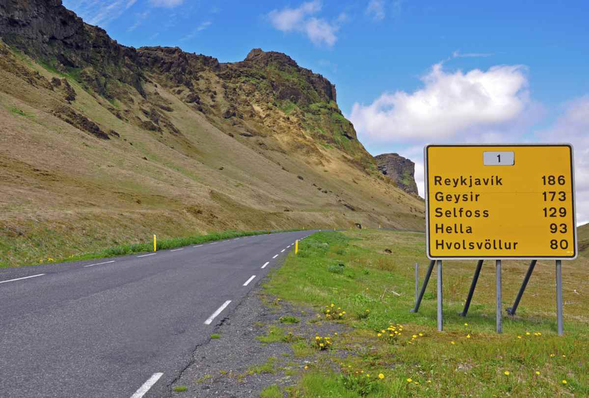 Isländische Landstraße mit gelbem Entfernungsschild nach Reykjavik und nahegelegenen Orten.