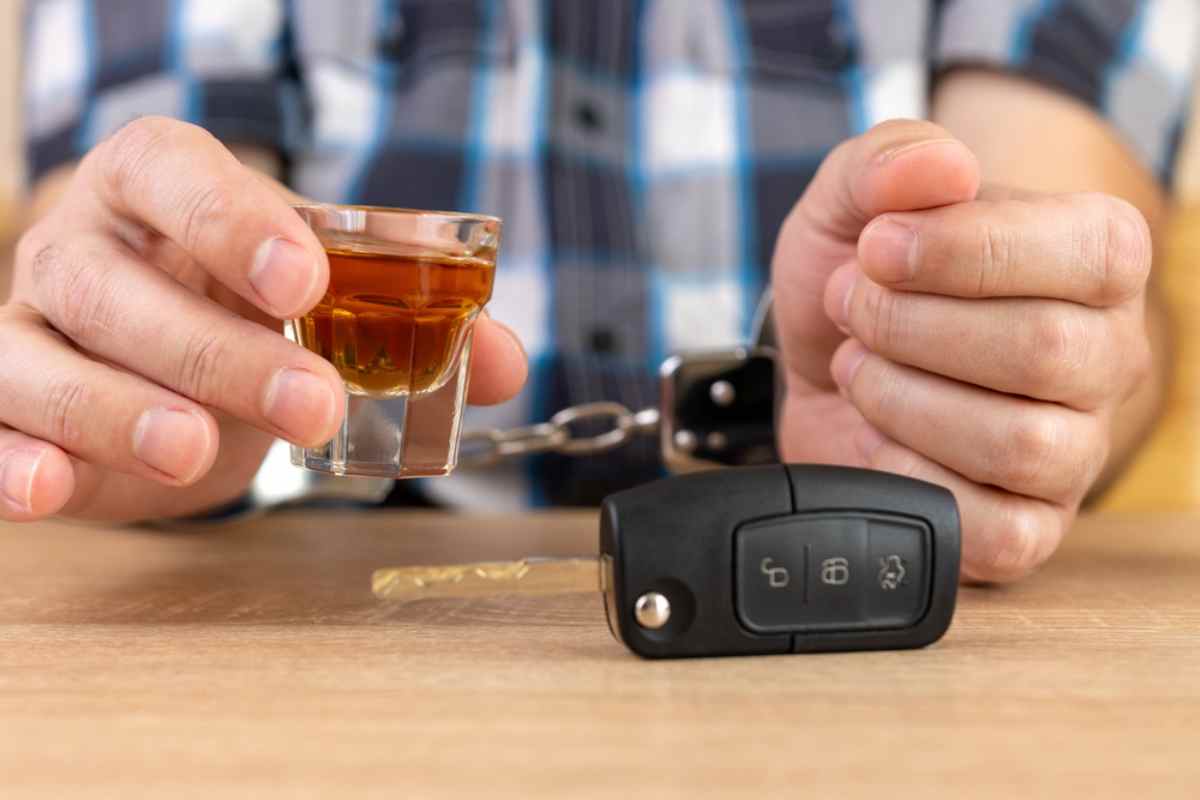 Nahaufnahme einer Person, die ein Glas Alkohol neben Autoschlüsseln hält, als Symbol für das Risiko von Trunkenheitsfahrten.