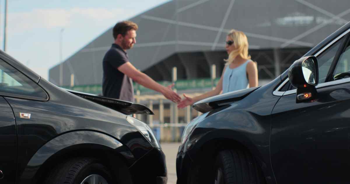 Zwei Fahrer schütteln sich nach einer Kollision vor beschädigten Autos die Hand.