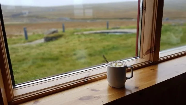 La mejor opción para conducir en islandia Imagen de un café cerca de una ventana donde se ve el paisaje islandés