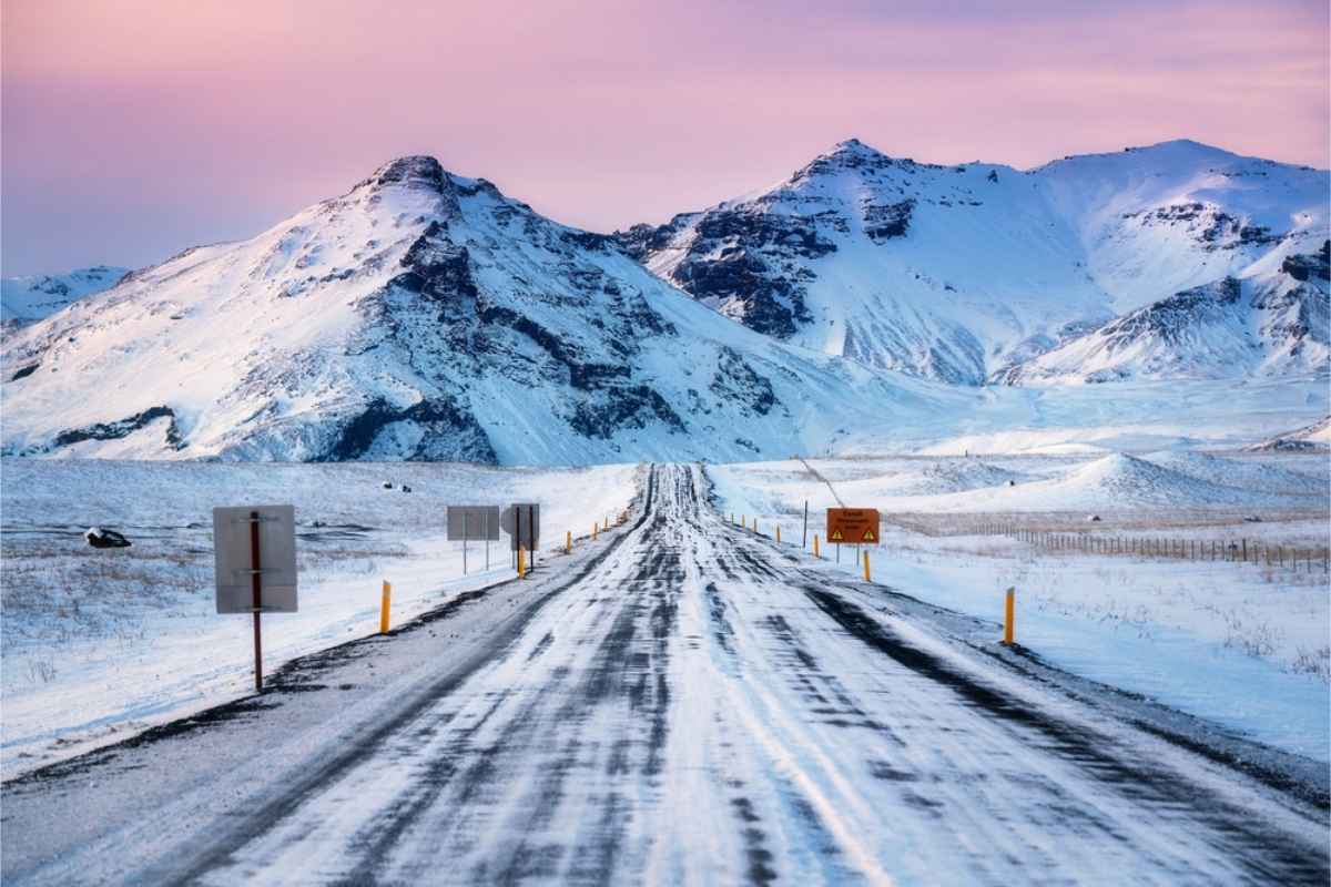 Carretera islandesa cubierta de nieve con un hermoso cordal montañoso al fondo