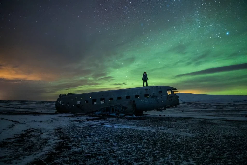 mujer de pie sobre la nave en Islandia con las luces del norte bailando arriba