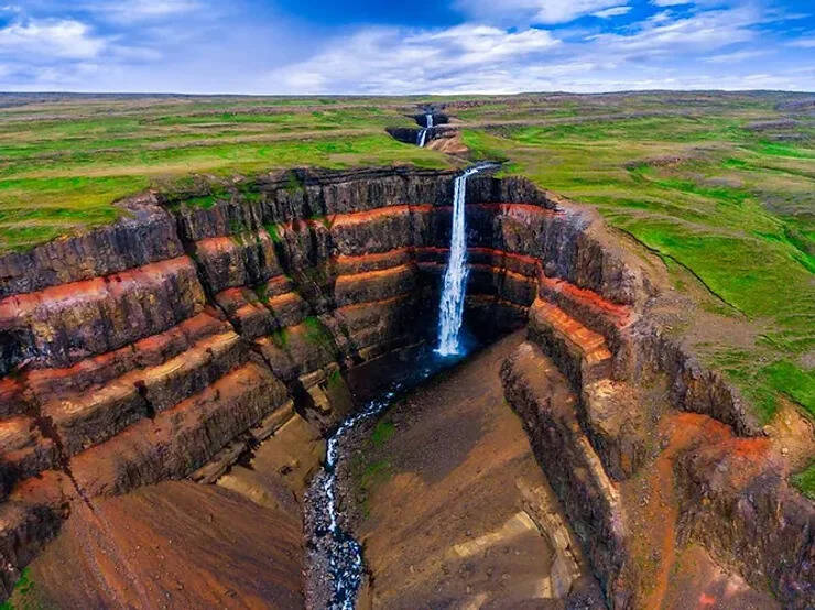 Vue aérienne de la cascade Hengifoss tombant dans une gorge aux parois rouges stratifiées en Islande.